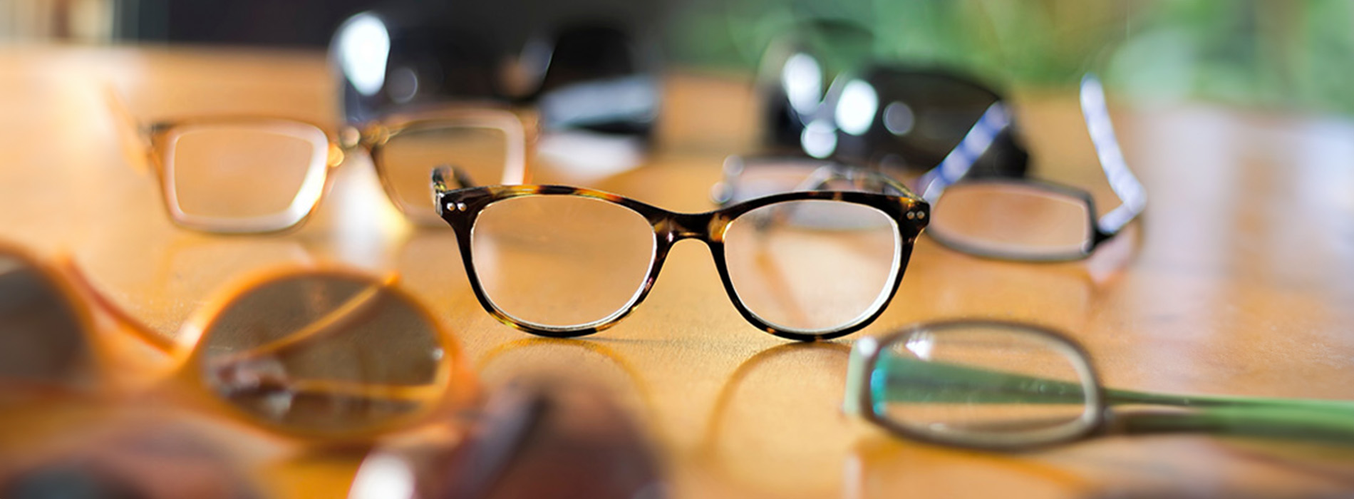 The image shows a collection of eyeglasses with various frame styles, placed on a table.