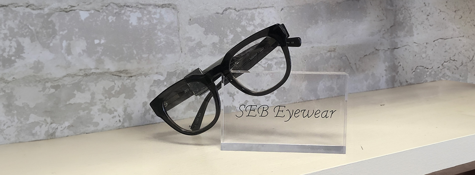 Eyeglasses with a black frame displayed on a clear stand.