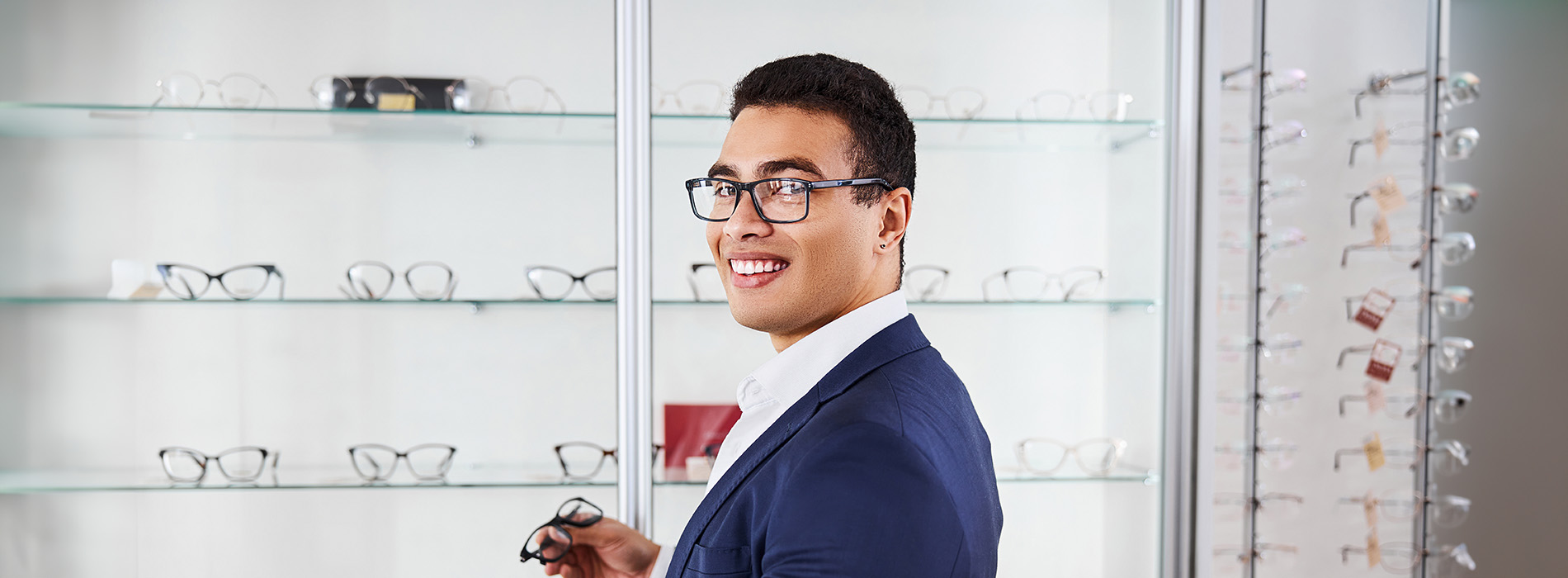 A man wearing glasses and a suit stands in front of an optical display.