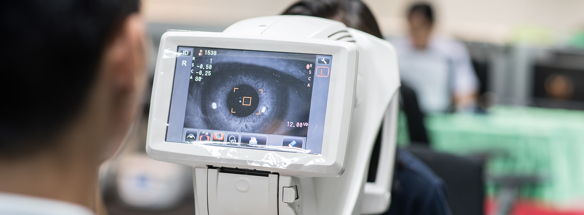 An eye exam machine with a person seated, displaying an image of the inside of a human eye on its screen.