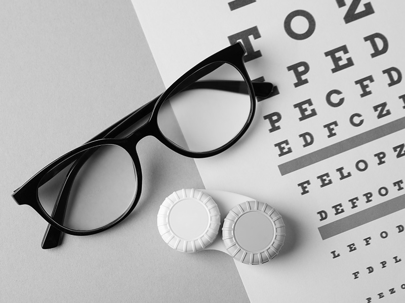 An optical prescription card and glasses with a magnified eye chart in the background.