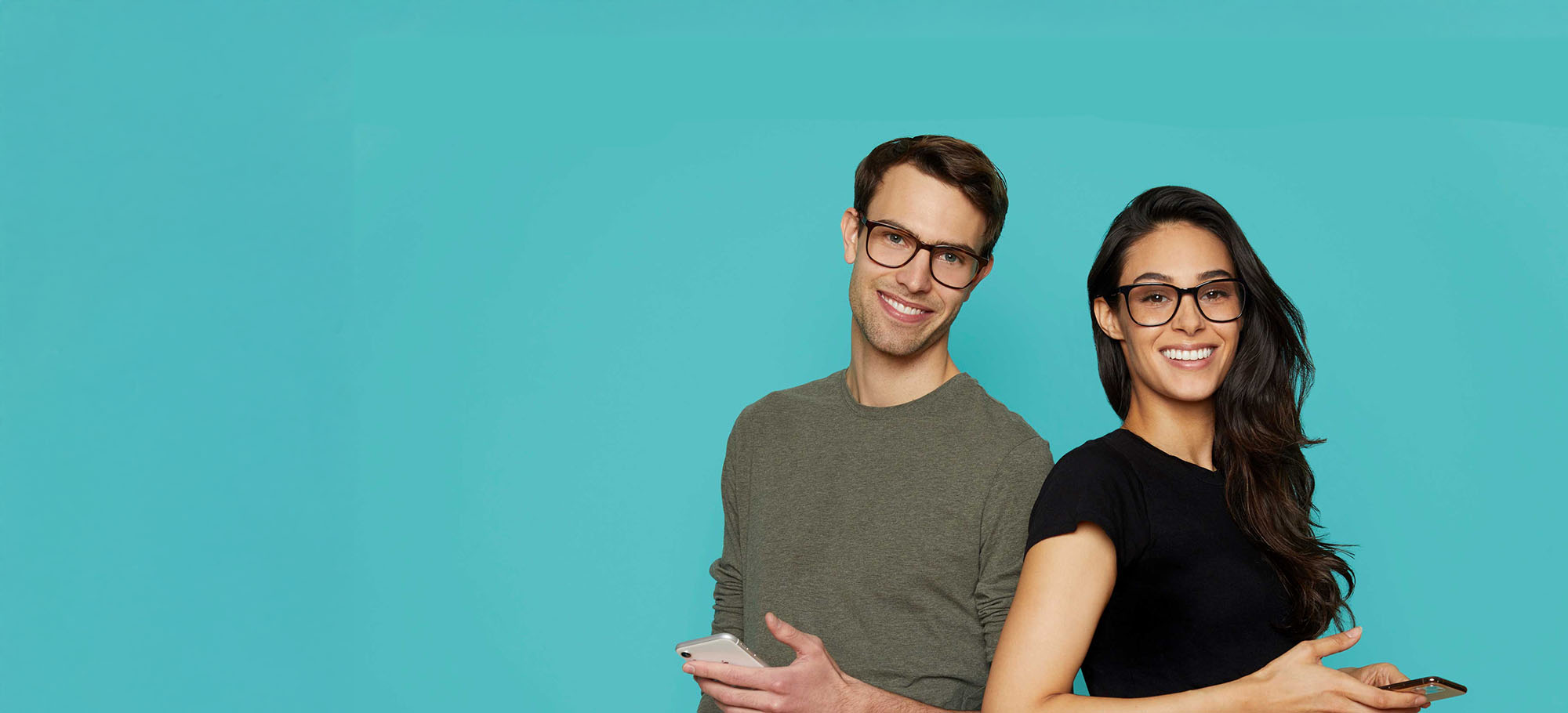 A man and a woman stand side by side, both smiling, against a plain background.