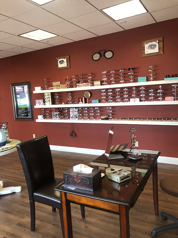 An optical store with a red wall, display shelves filled with glasses and frames, and a desk in the foreground.