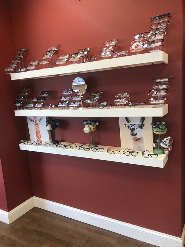 The image depicts a wall-mounted display shelf with various pairs of eyeglasses and frames.