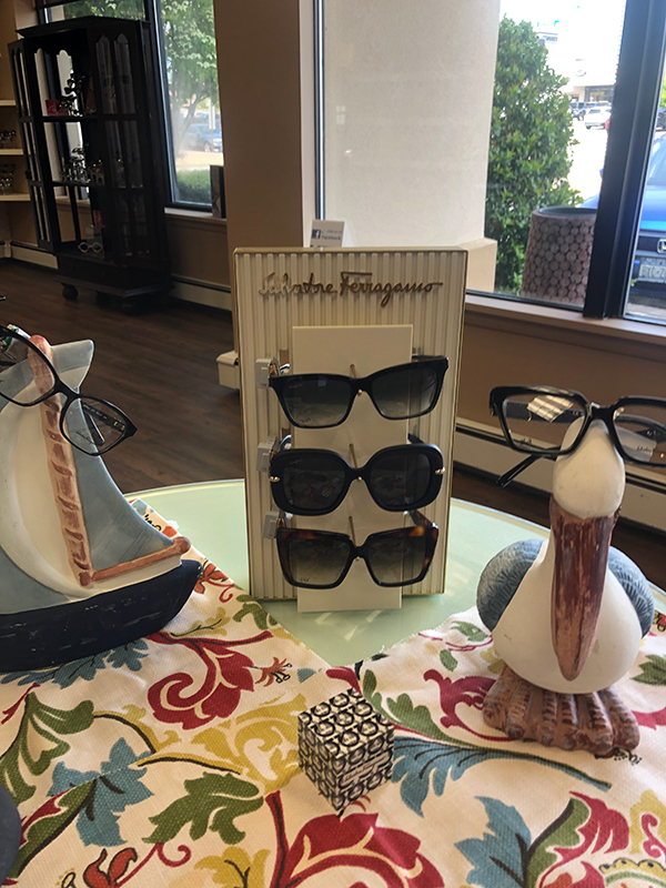 The image shows a display of sunglasses and a pair of eyeglasses, with two figurines, one resembling a cat and the other a bird, placed in front of it.