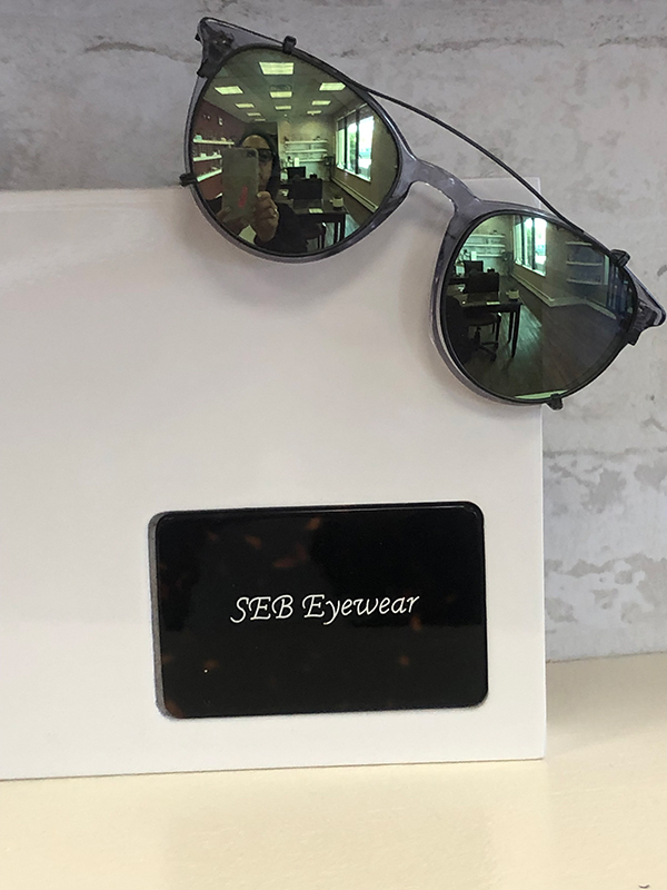 A pair of sunglasses with a brand logo on the box, placed against a blurred background.