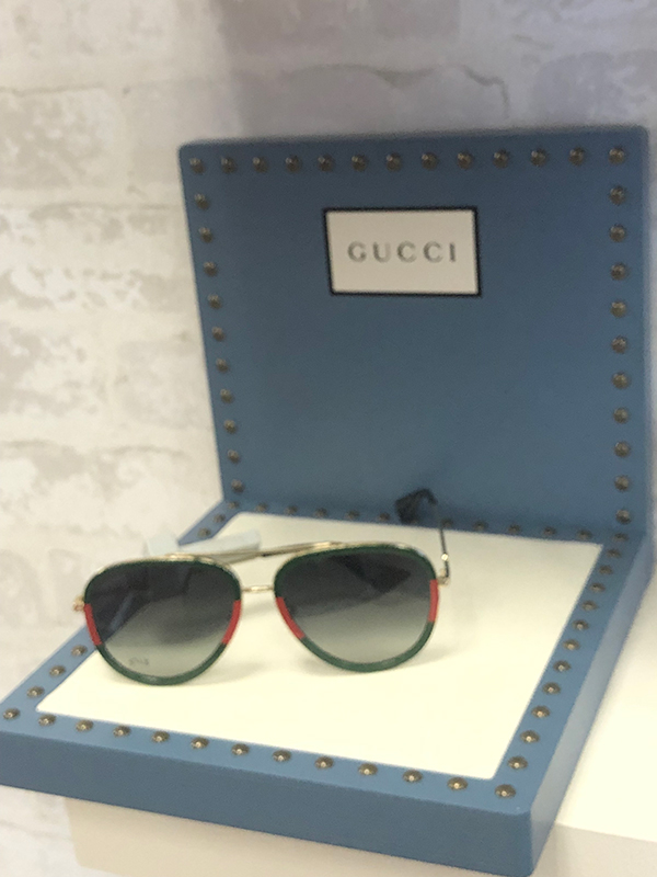 A pair of sunglasses with a red accent, placed in an open blue box with the brand name  Gucci  visible.