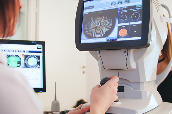 A person is using an eye exam machine, focusing on a screen displaying what appears to be an optical scan of a human eye.