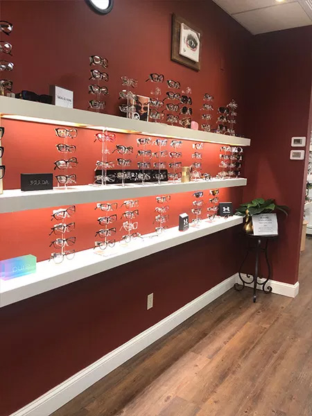 An optical store with a display of eyeglasses on shelves, set against a red wall.