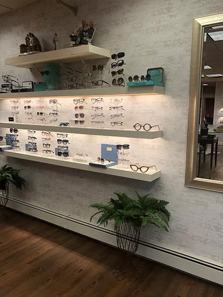 An optical store display with various eyeglass frames and cases, set against a white wall with a framed mirror above.