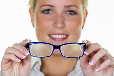 A woman wearing blue glasses holds them up to her face.