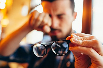 The image shows a man holding a pair of eyeglasses up to his face, with an expression of surprise or shock.