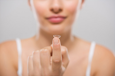 The image features a close-up of a person s hand holding a clear, circular object that resembles a contact lens or an eye exam tool.