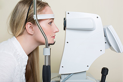 An individual with blonde hair wearing a headset, sitting in front of an eye exam machine.