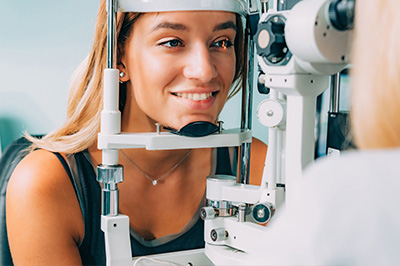 A young woman is seated in front of a vision testing machine, wearing an eye patch over one eye.